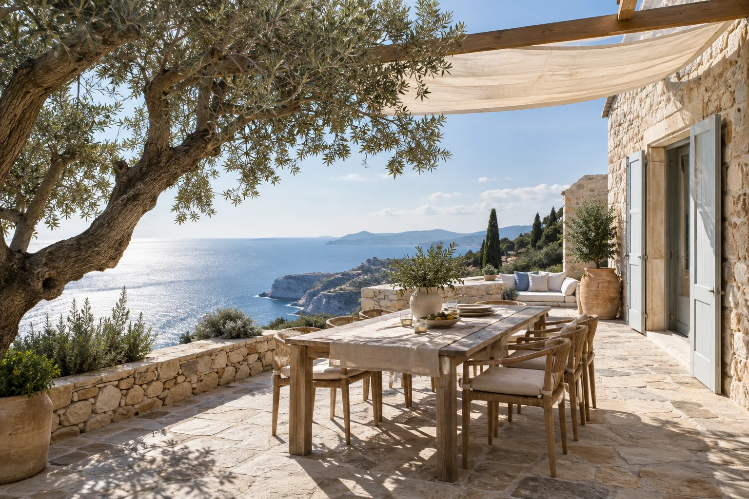 A stone villa terrace beneath an olive tree overlooking the sea